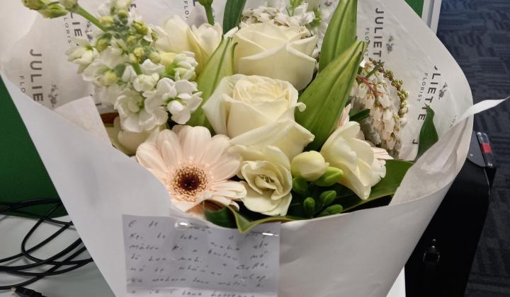 A bunch of flowers in green, white and peach wrapped in white paper.