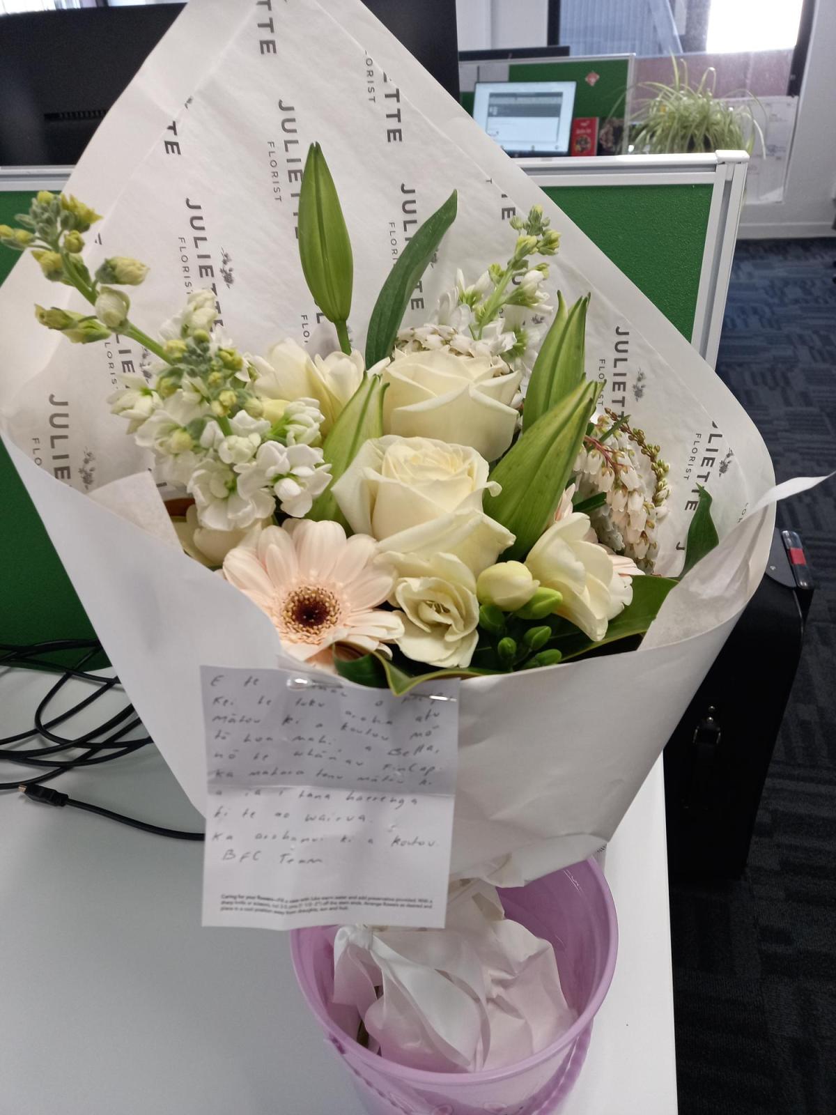 A bunch of flowers in green, white and peach wrapped in white paper.